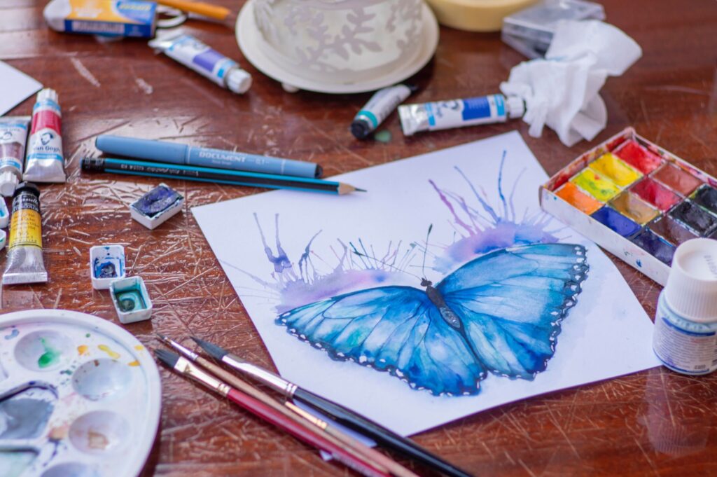 Drawn and painted butterfly with paints and paintbrushes lying around