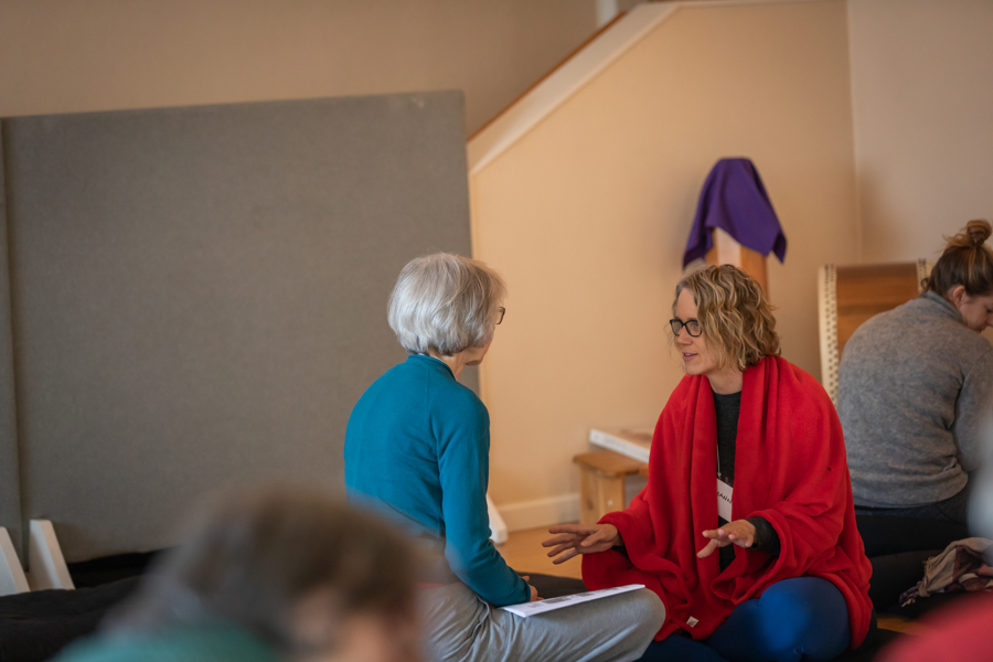 Two mindfulness students sitting on the ground inside the dharma hall, deep in discussion about their experience with a meditation.