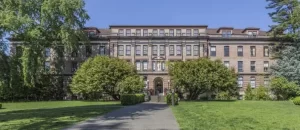 The exterior of the Good Shepherd center in Seattle. A four story brick building with steps up to the entrance and large rhodedendron bushes on their side of the entry.