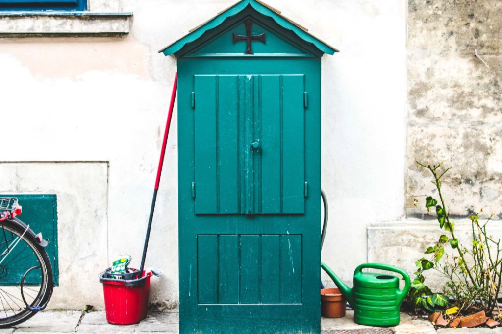 A small green-blue shed against a white wall
