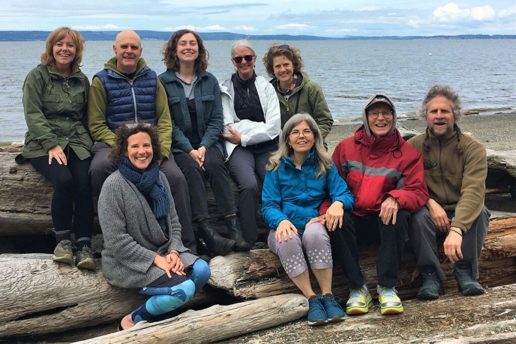 Mindfulness Northwest staff members pictured sitting on driftwood with water and sky in the background