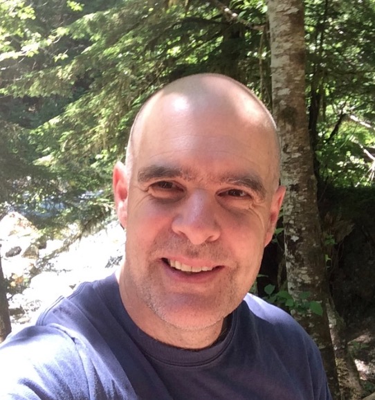 A selfie of Tim Burnett, smiling on a hiking trip in the Cascade Mountains of Washington.