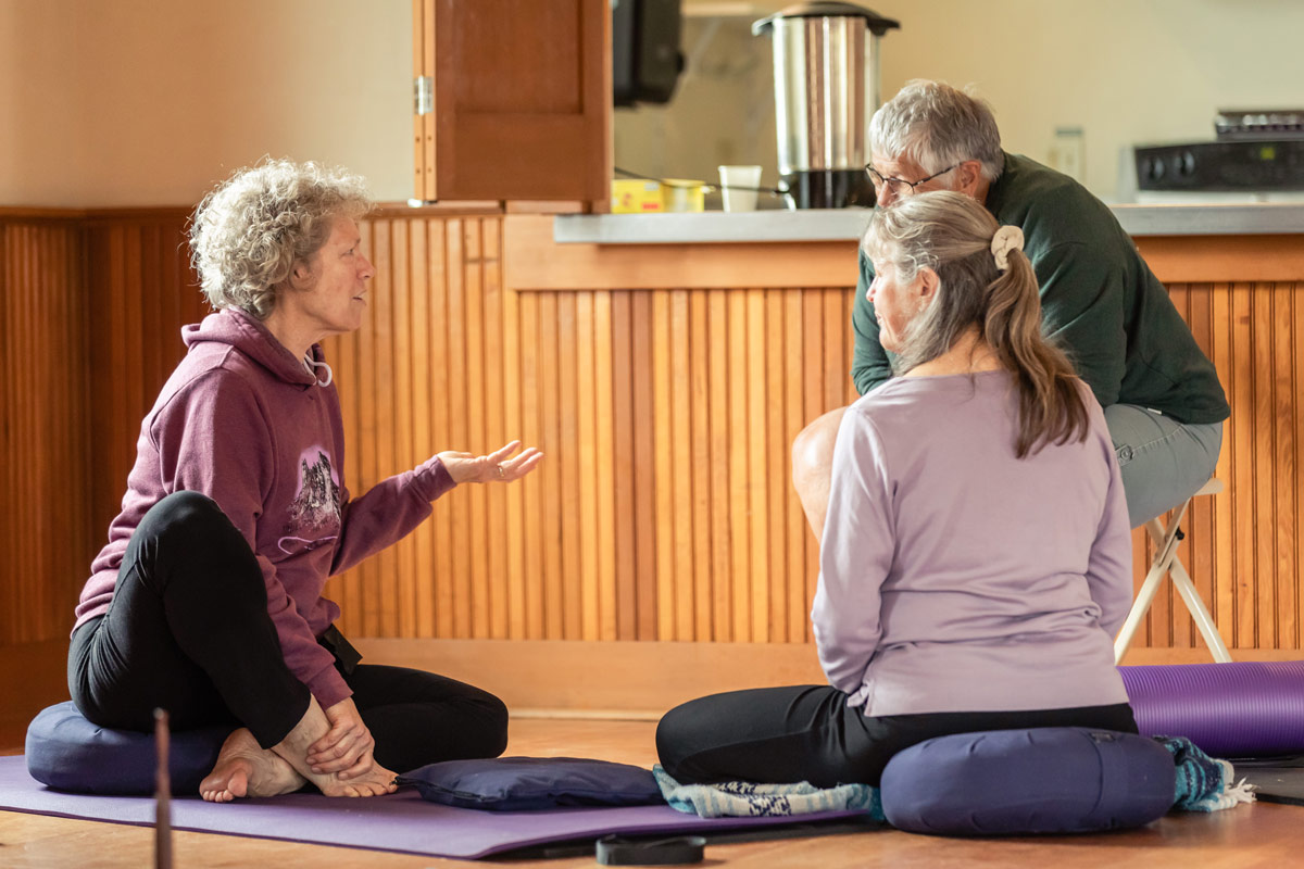 A woman in a purple sweatshirt sits on the ground in a circle in conversation with two other participants.