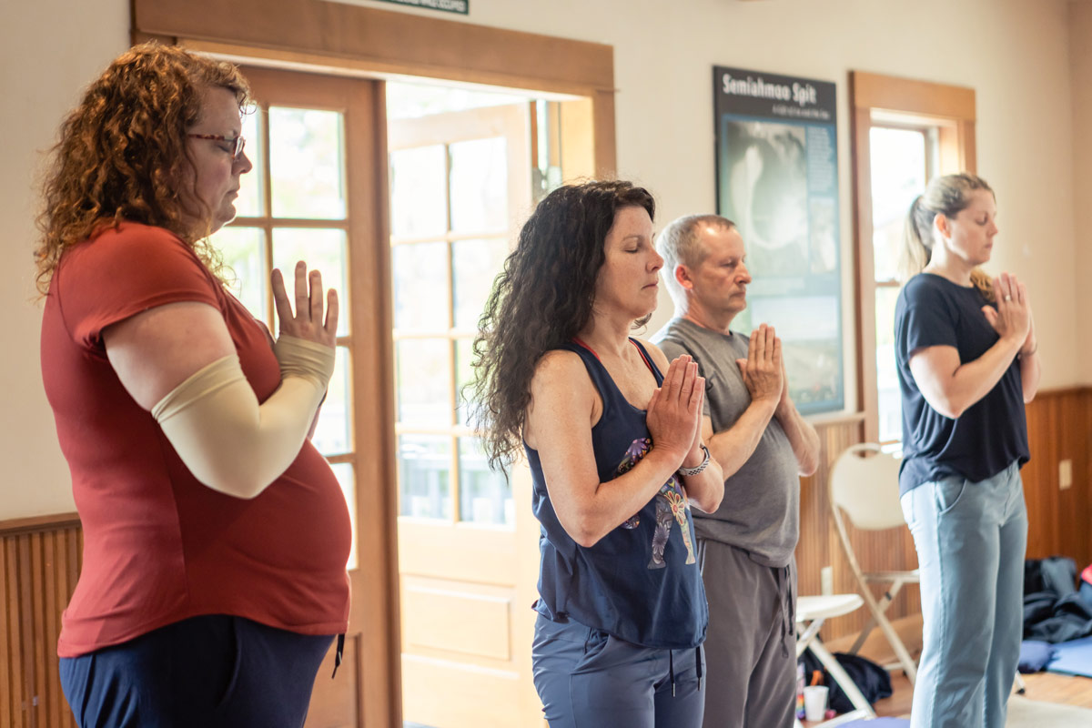 Four students standing with hands in the prayer position and eyes closed. 