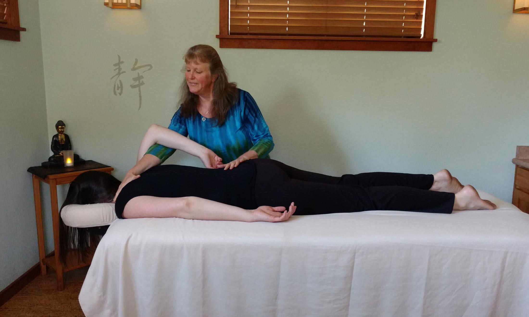 Raizelah Bayen giving a mindful massage to a person laying face down on a massage table wearing black pants and tank top. 