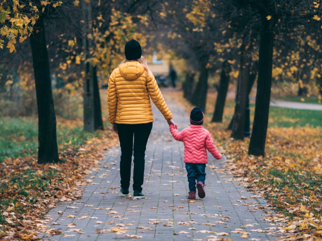 Mom & child walking away down leafy sidewalk