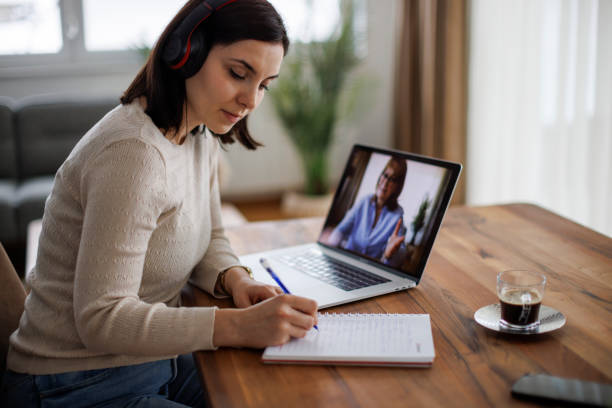 Young focused woman learning online, writing notes during a virtual lesson